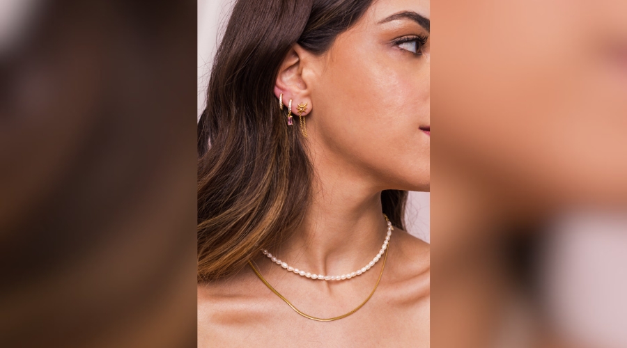 Close-up of a beautiful young woman's neck wearing a pearl necklace and a snake chain and gold earings hang from woman's ear