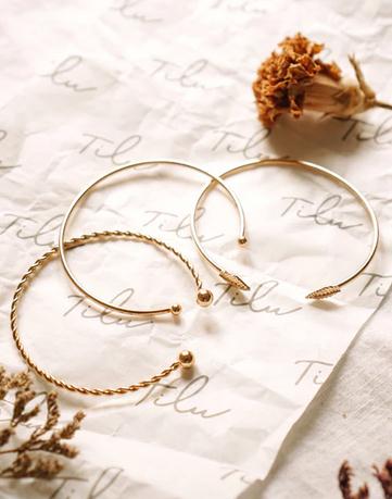 Image of three gold-colored bangles with flowers on a simple background
