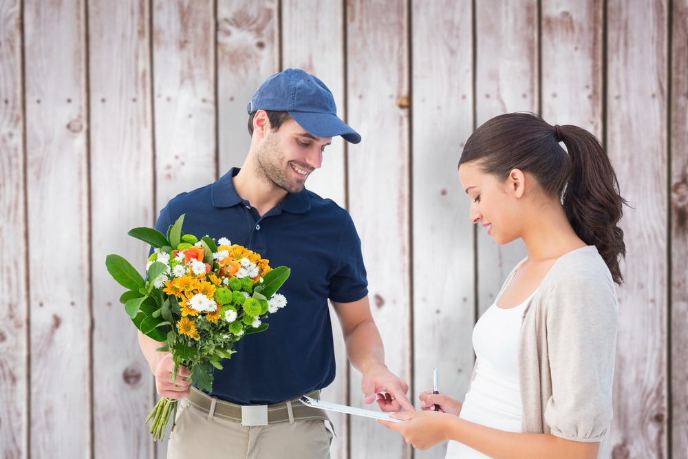 Happy flower delivery man with customer against wooden planks