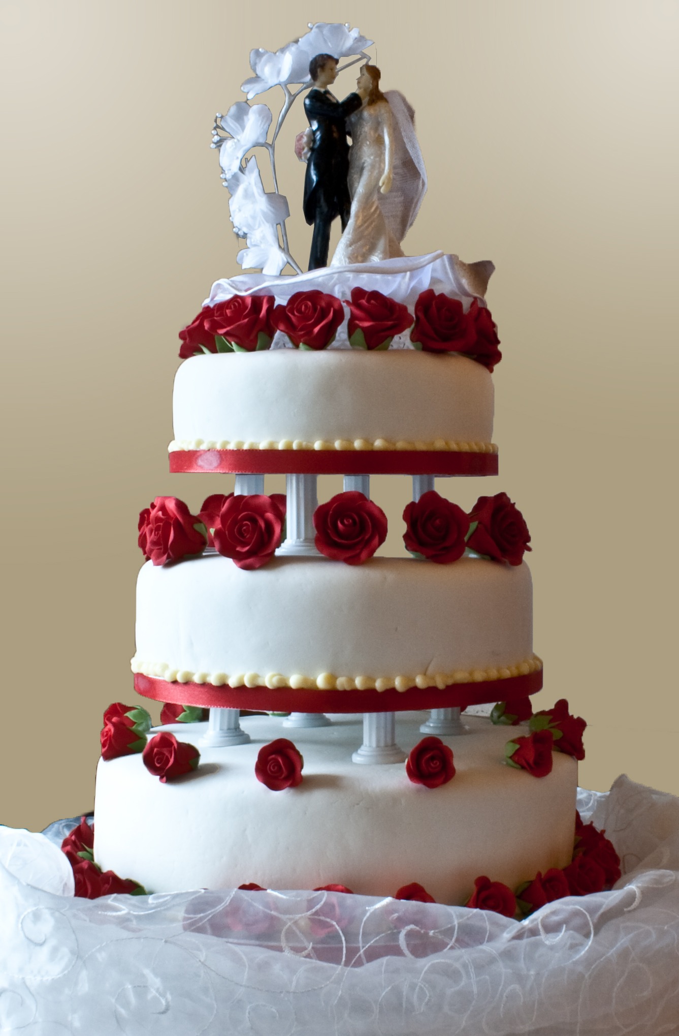 A three-layer wedding cake with pillar supports and “topper” figures