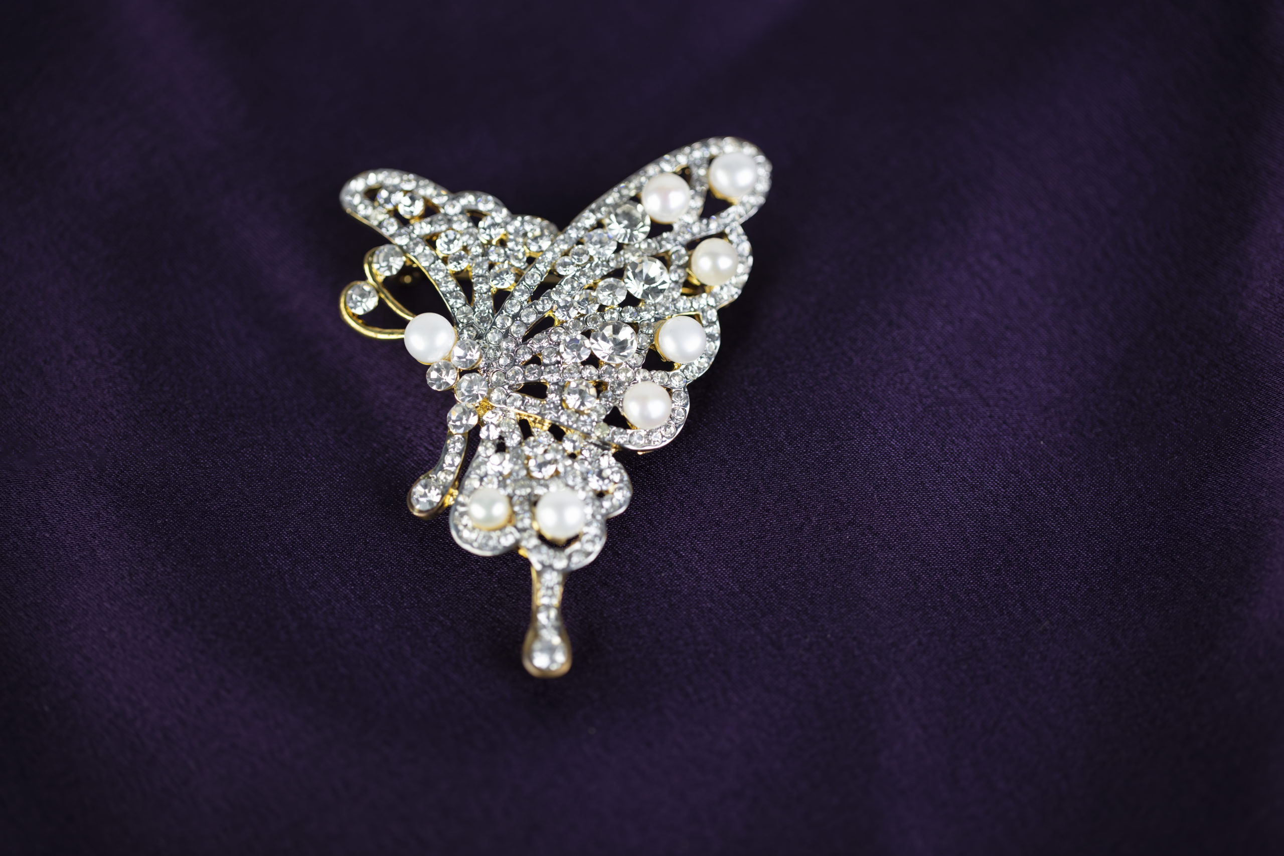 Pearl and diamond brooch in the shape of a butterfly isolated on a dark purple silk background